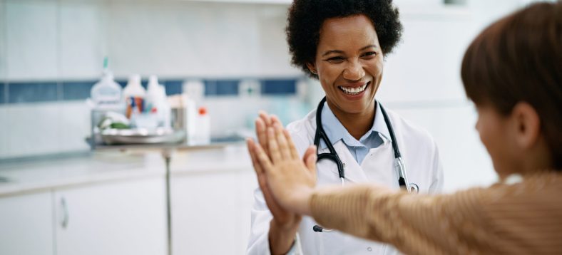 Happy African American pediatrician giving high five to a kid after medical examination at doctor's office.