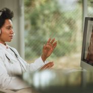 Shot of an African female doctor having video call with patient on computer in her consulting room during COVID-19 pandemic.